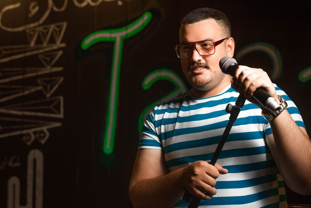Stand-up comedian in a striped shirt holding a microphone on stage