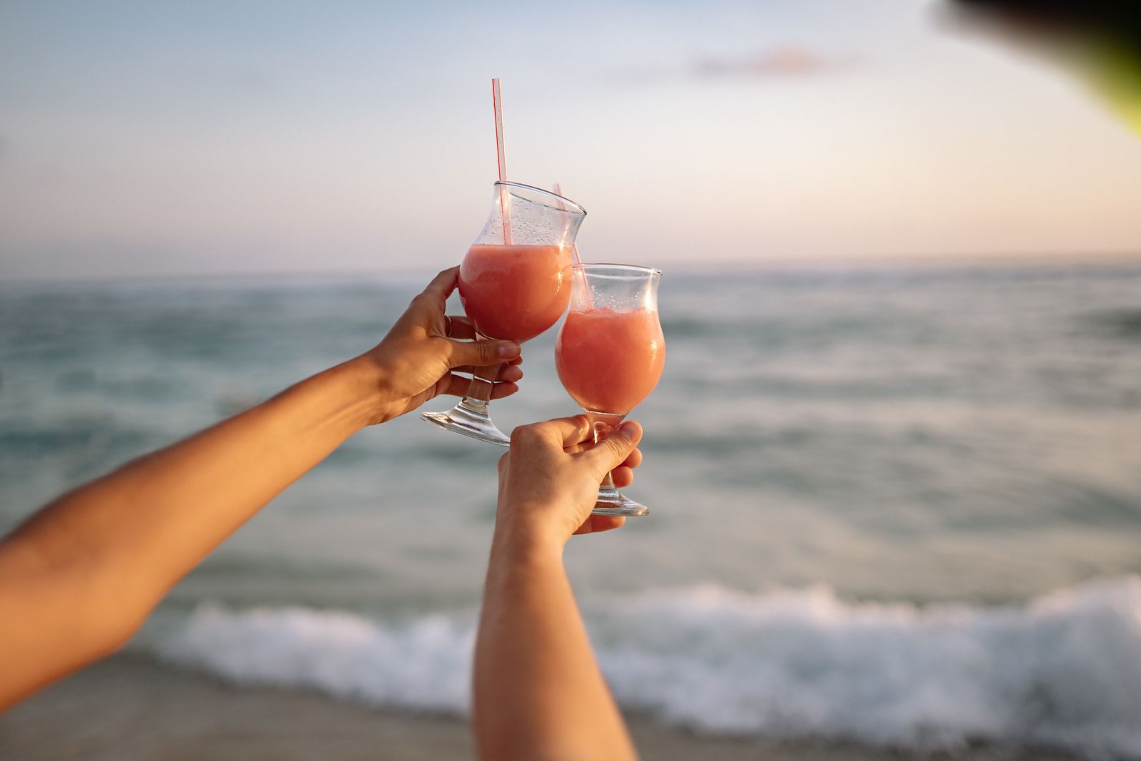 Two tropical cocktails raised in a toast by the sea at sunset, happy hour cruise style