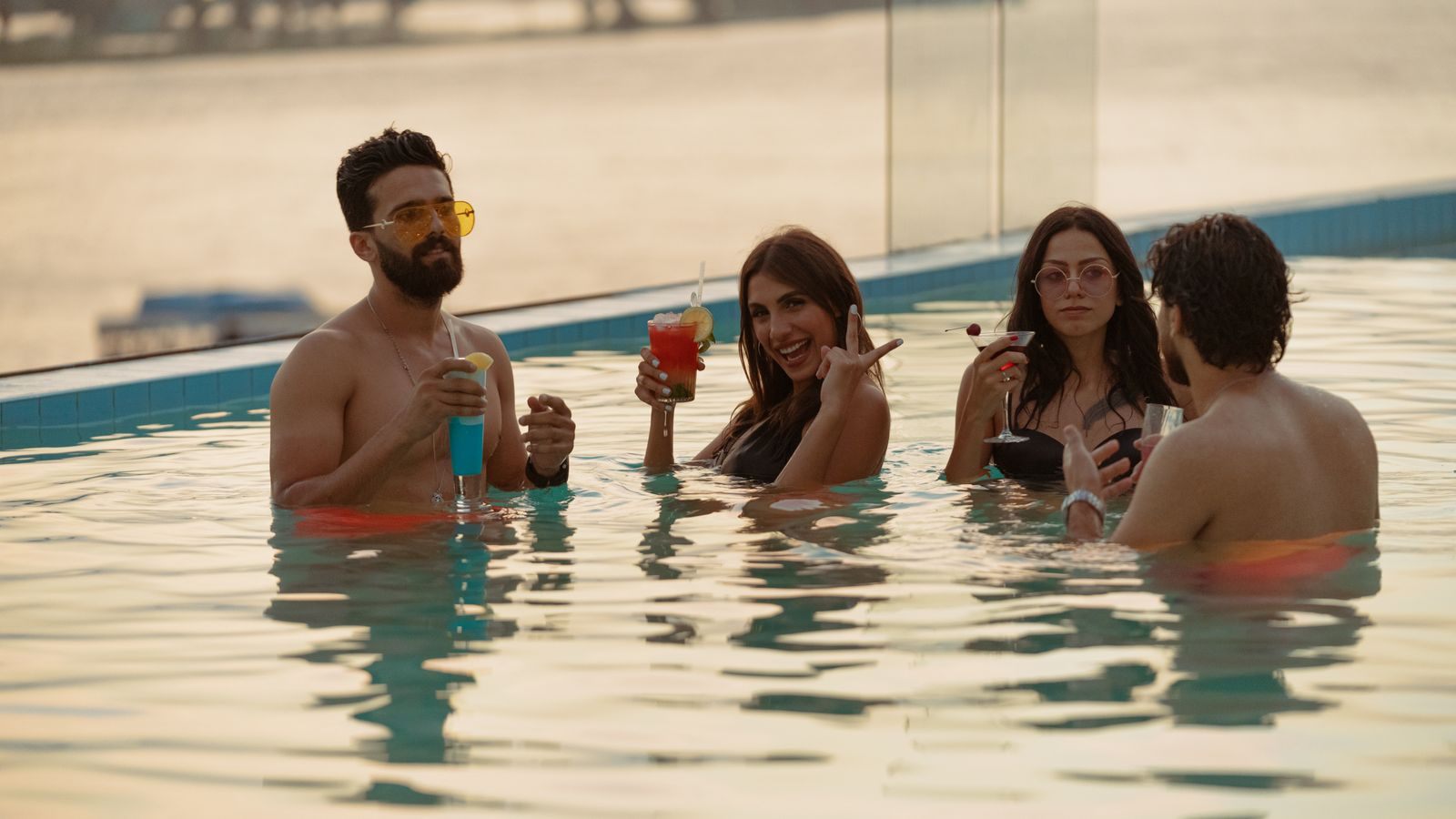 Friends laughing with cocktails in an infinity pool, the mood of fun cruises