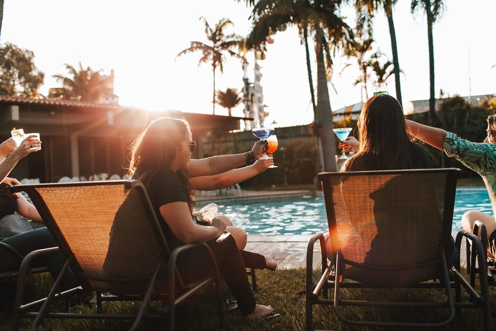 Friends relaxing on deck chairs with drinks by a pool at sunset
